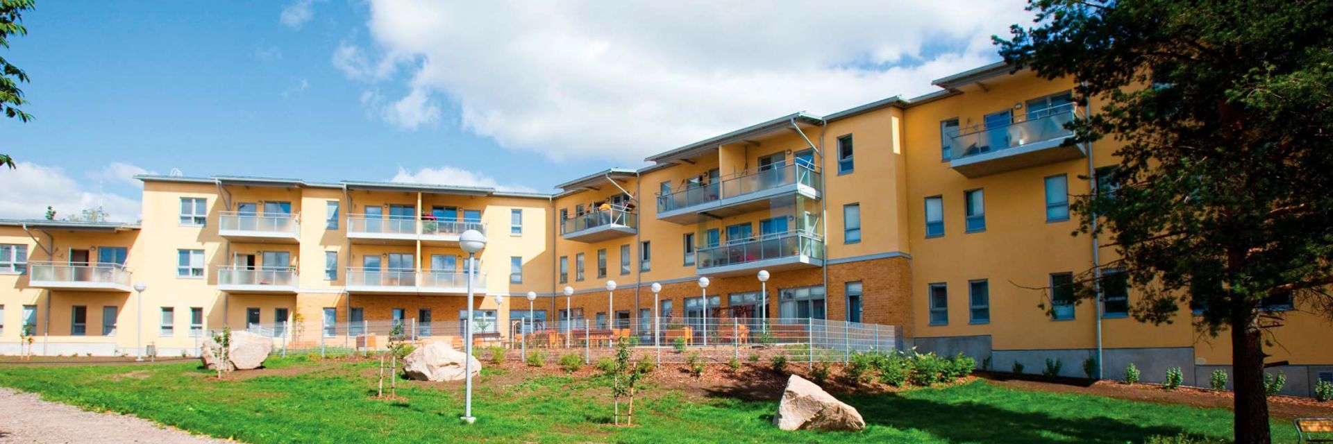 Servicehuset Elsie, en flervåningsbyggnad med balkonger och en grön gård framför byggnaden.